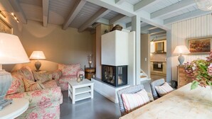 A cozy living room with a fireplace, floral sofa, and a dining area. - Bauernkate Liepe (Rankwitz)