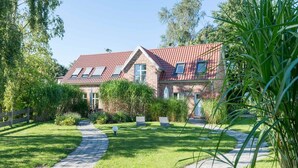 A two-story house with a red-tiled roof, a brick facade, and a paved garden path leading to the entrance. - Bauernkate Liepe (Rankwitz)