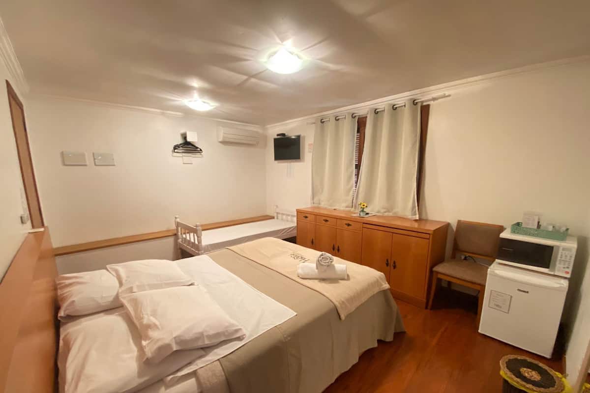 A hotel room with a bed, a desk, a chair, a microwave, and a trash bin.