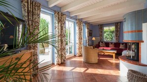 A living room with a sofa, a table, and a fireplace. There are curtains on the windows, and a plant is visible. - Reetdachhaus in Krienke (Rankwitz)