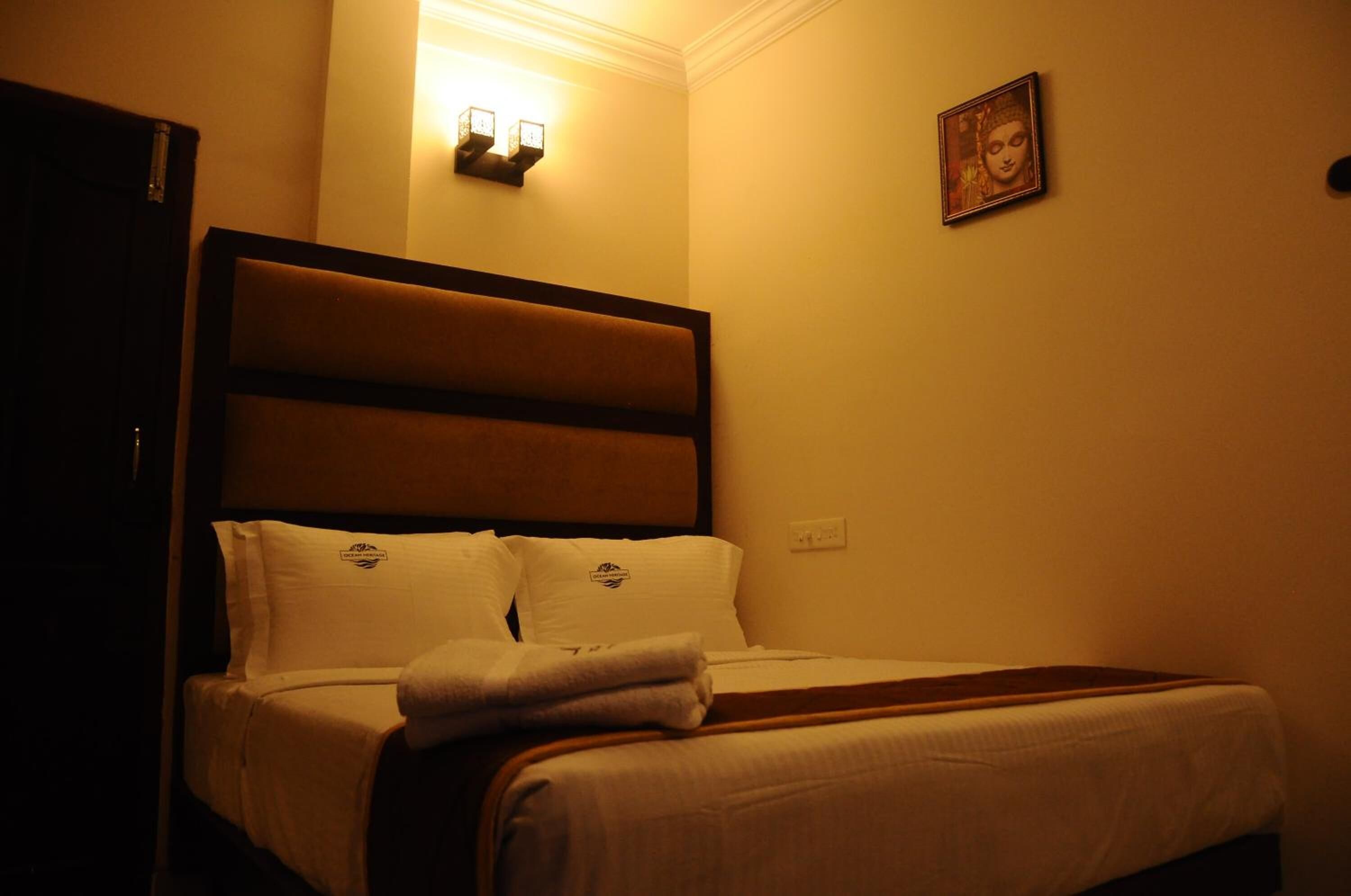 A hotel room with a large bed, two wall-mounted lights, a framed picture, and a door.