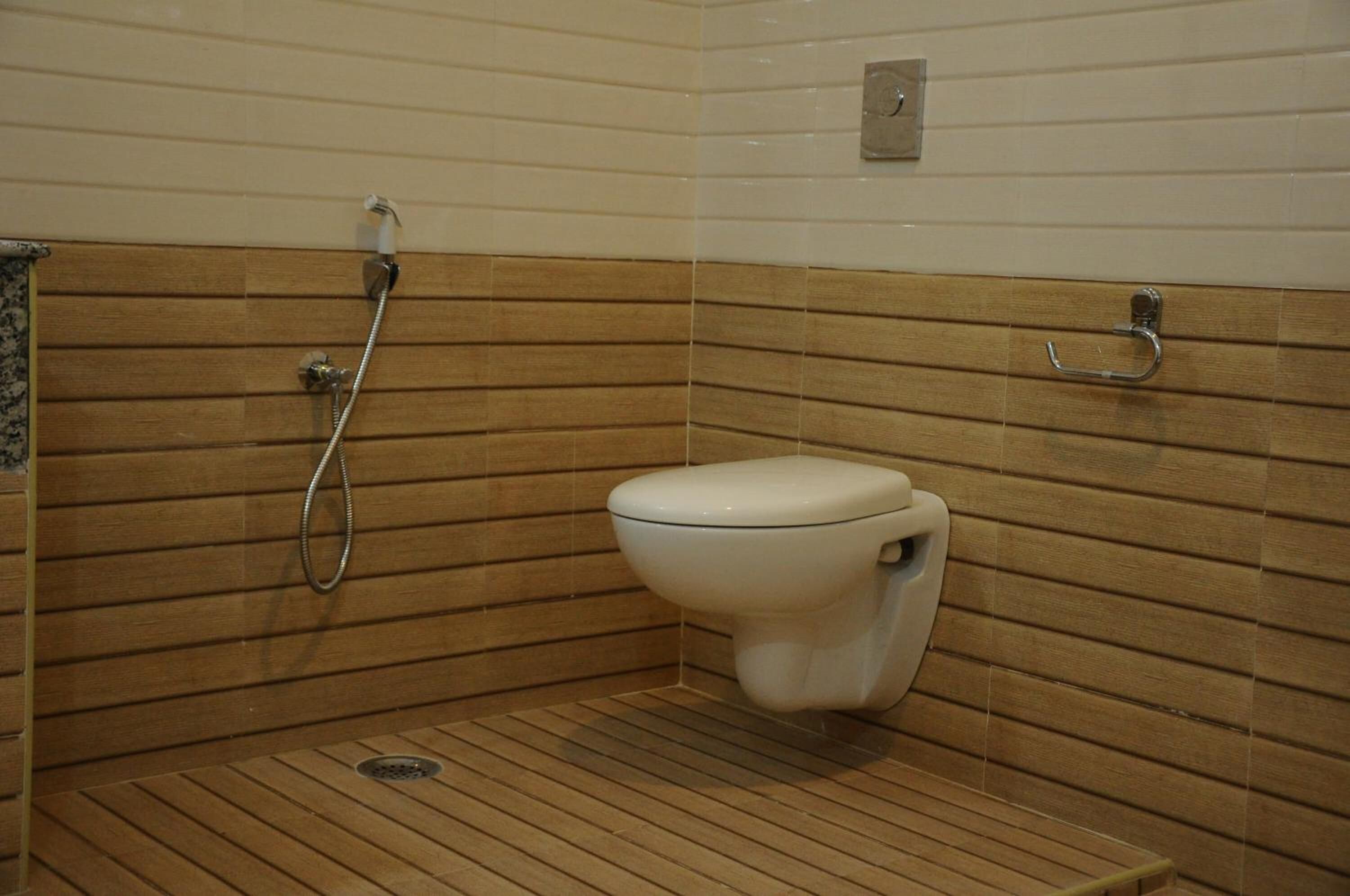 A small, wooden-floored bathroom with a toilet and a shower.