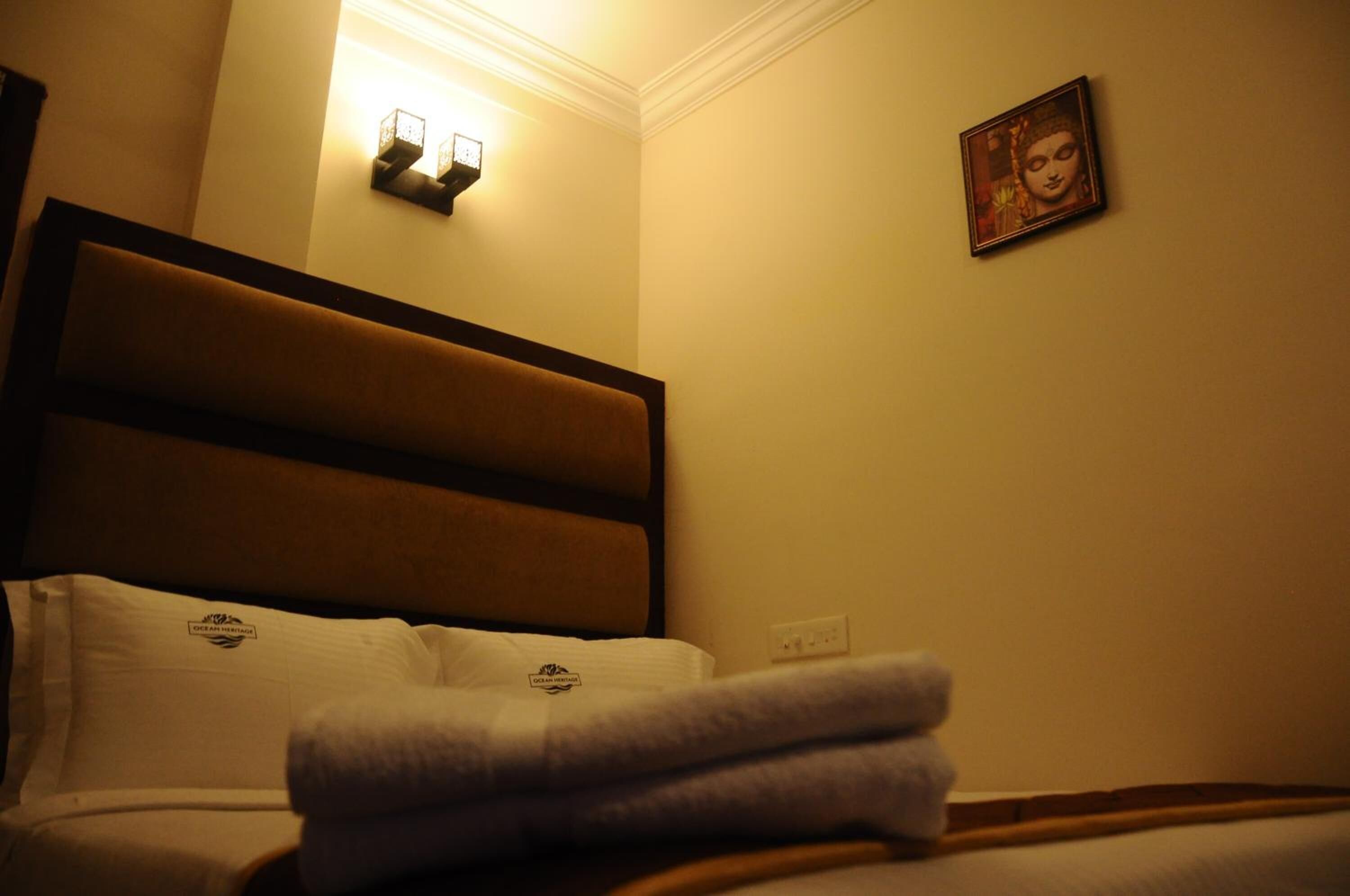 Een hotelkamer met een bed, hoofdeinde, een aan de muur bevestigde lamp en een ingelijst schilderij.