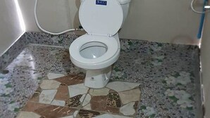 A toilet with a white seat and lid, a white pipe, and a tiled floor with a geometric pattern. - Lanta Local Hut (Ko Lanta)
