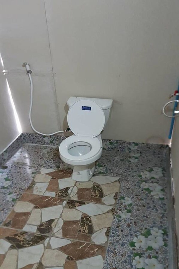 Un inodoro con asiento y tapa blancos, una tubería blanca y un suelo de baldosas con un diseño geométrico.