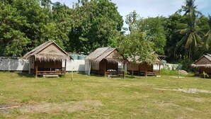 A row of thatched-roof huts with wooden benches in front, surrounded by lush greenery and trees. - Lanta Local Hut (Ko Lanta)
