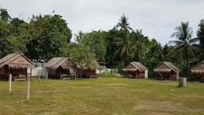 A row of thatched-roof huts in a grassy area with palm trees in the background. - Lanta Local Hut (Ko Lanta)