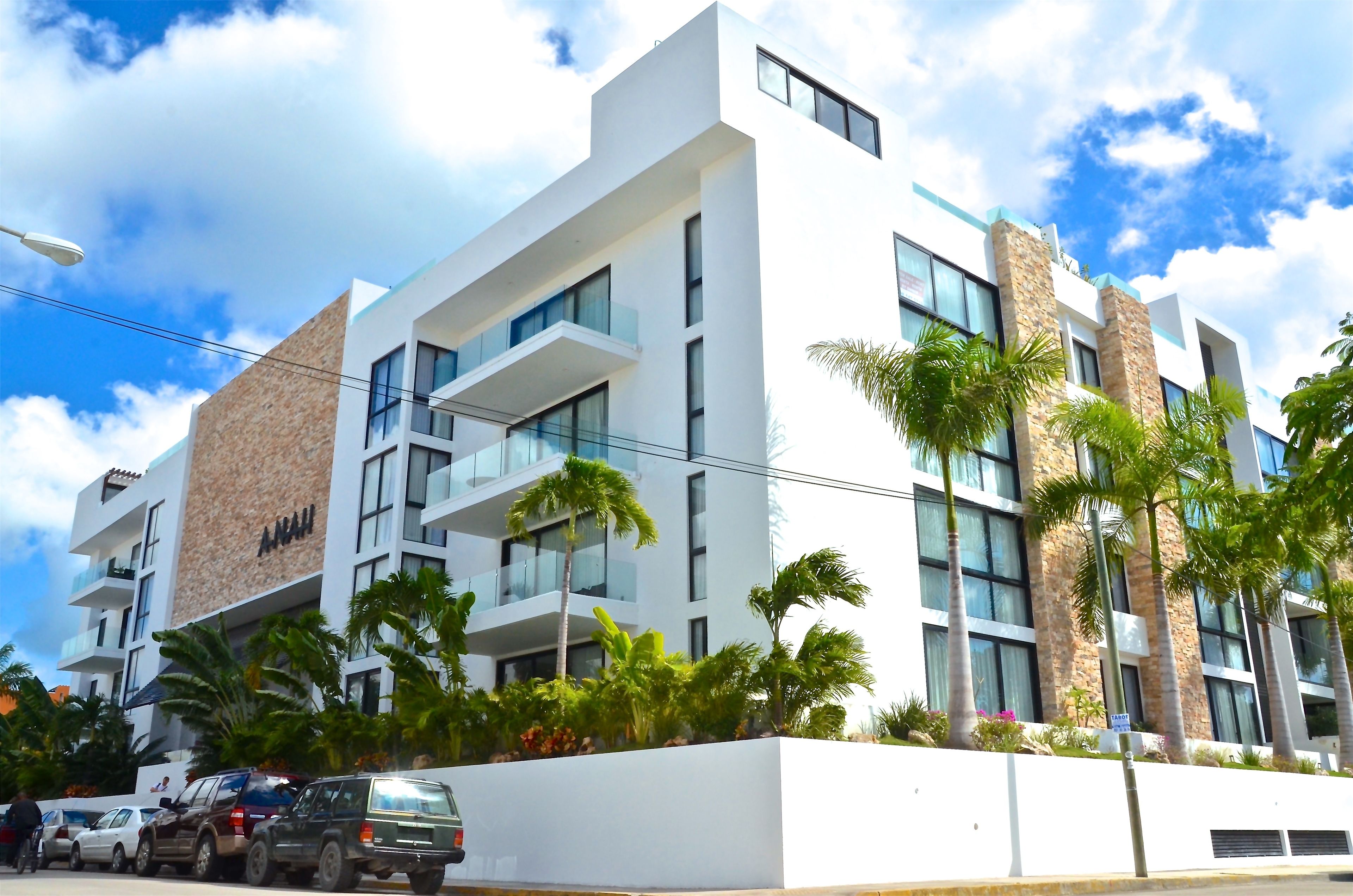 A modern hotel with a white facade, multiple balconies, and palm trees in the foreground.