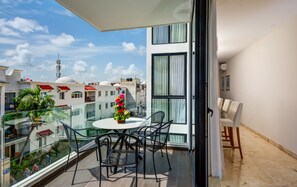 A balcony with a glass railing, a table with chairs, and a vase of flowers.