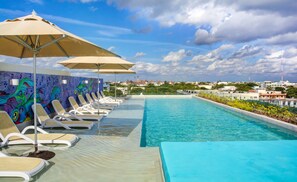 A swimming pool with lounge chairs and umbrellas, a colorful mural, and a view of buildings in the background.