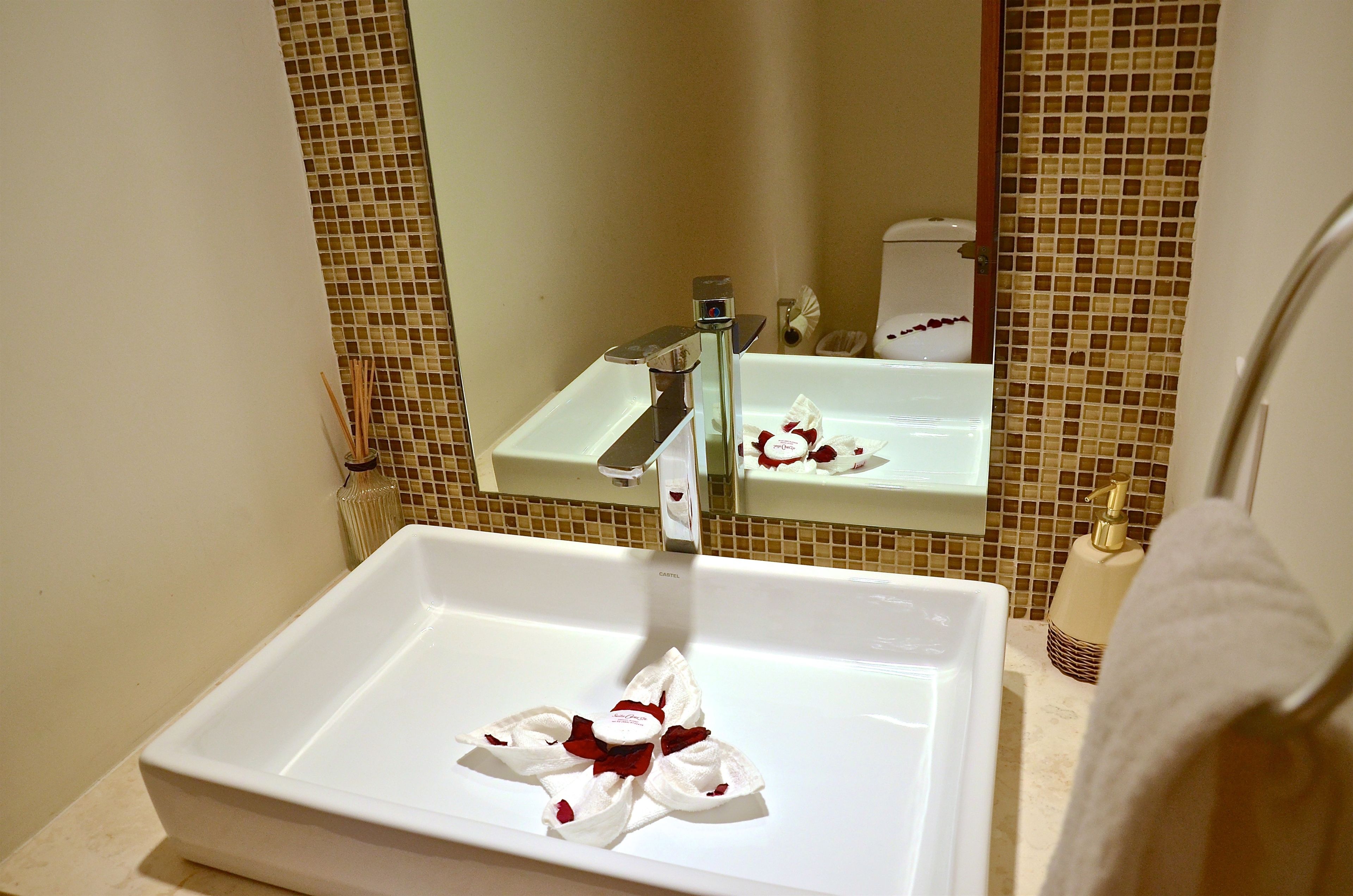 Une salle de bain avec un lavabo blanc, un miroir et un mur recouvert de carreaux.