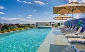 A clear blue pool with lounge chairs and umbrellas, surrounded by a low wall with a mural of fish. - A-Nah Suites Apartamentos by CSR (Playa del Carmen)