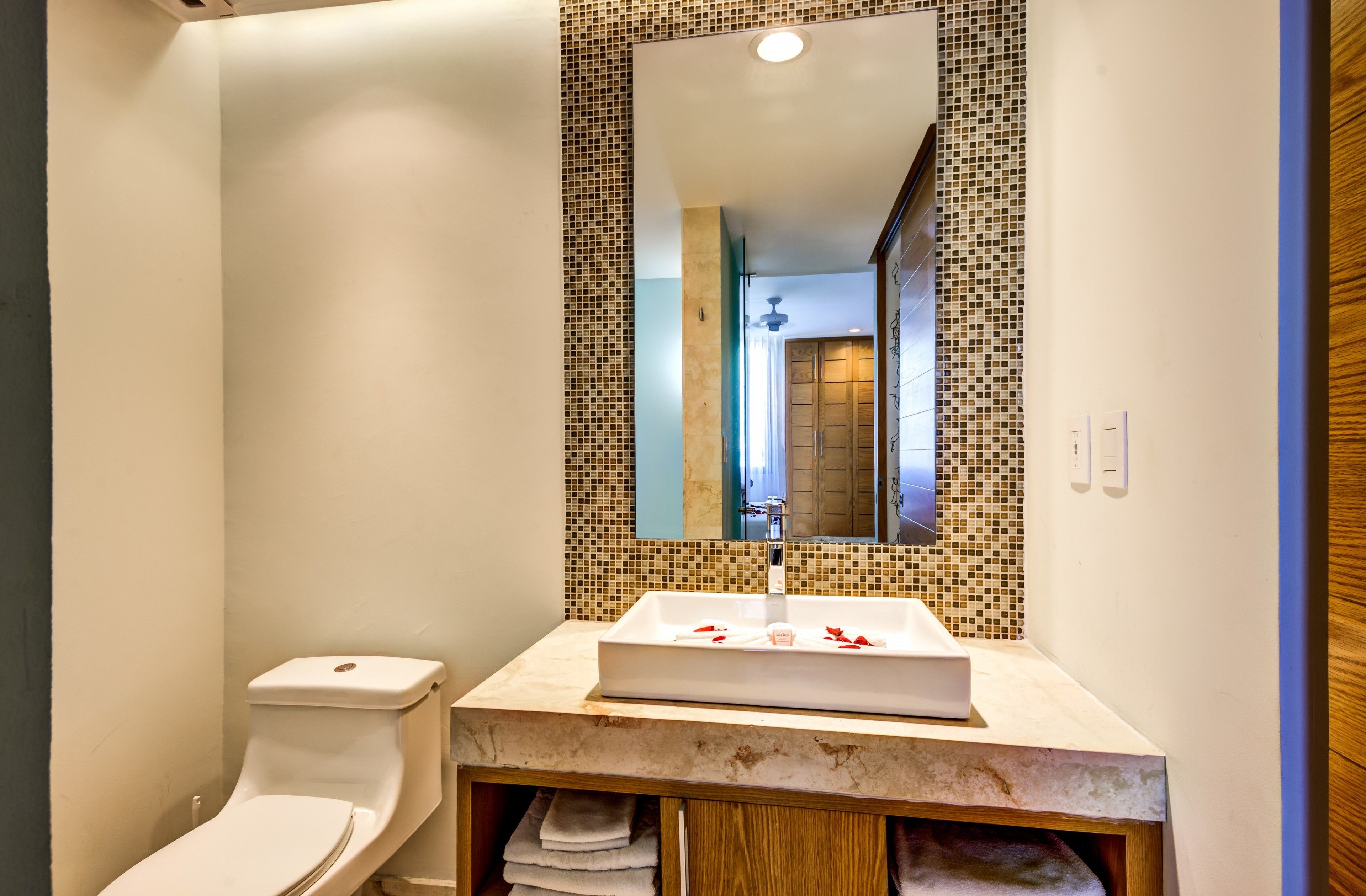 Une salle de bain comprenant des toilettes, un lavabo avec un miroir au-dessus, et un mur recouvert de carreaux.