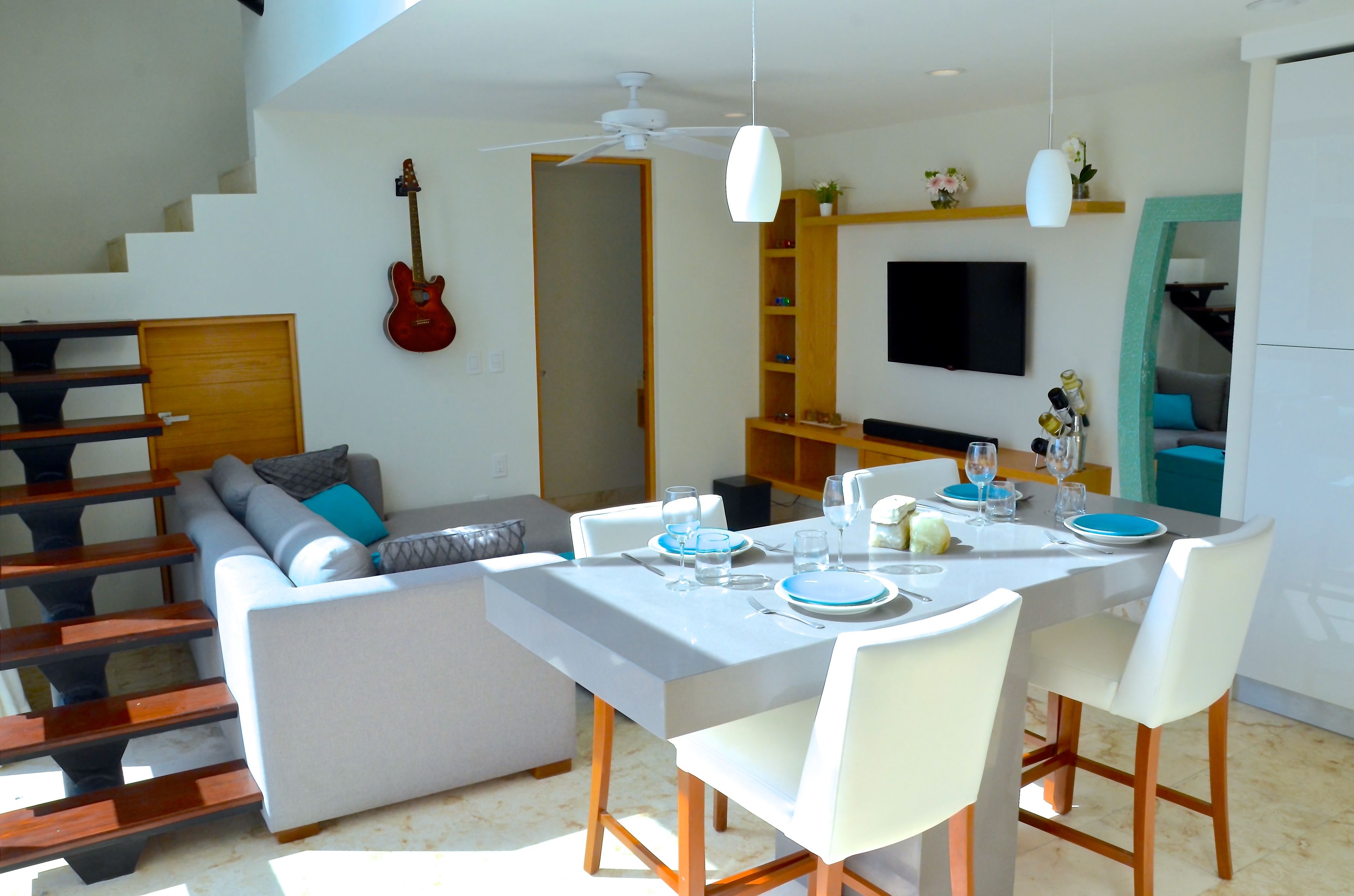 Um espaço de estar moderno com área de jantar, escada e uma guitarra pendurada.