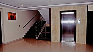 A spacious lobby with a polished tile floor, a staircase with a metal railing, and a marble elevator. - Hotel mookambika palace (Kundapur)