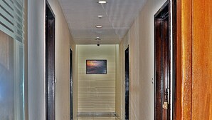A corridor with a polished floor, doors on both sides, and recessed lighting on the ceiling. - Hotel mookambika palace (Kundapur)