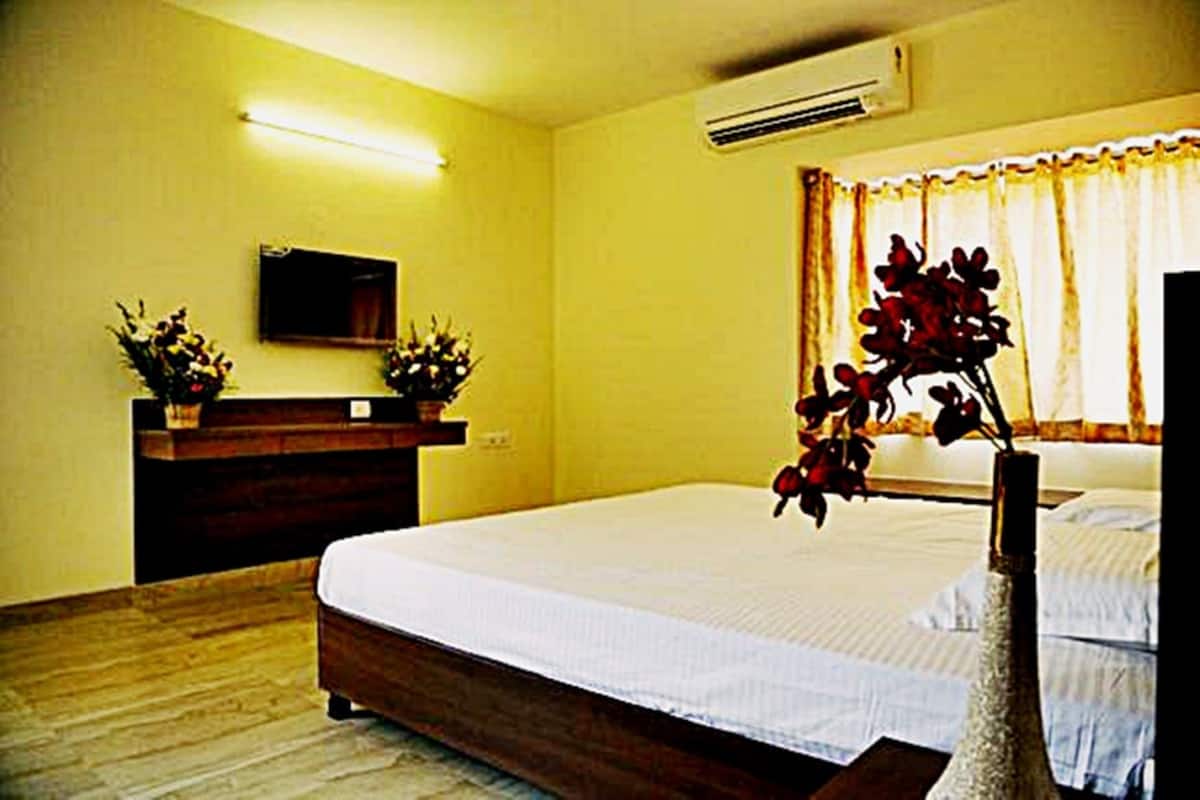 A hotel room with a bed, a flat-screen TV mounted on the wall, a wooden dresser, and a window with curtains.