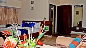 A hotel room with a bed, a sofa, a coffee table, and a decorative plant. - Hotel mookambika palace (Kundapur)