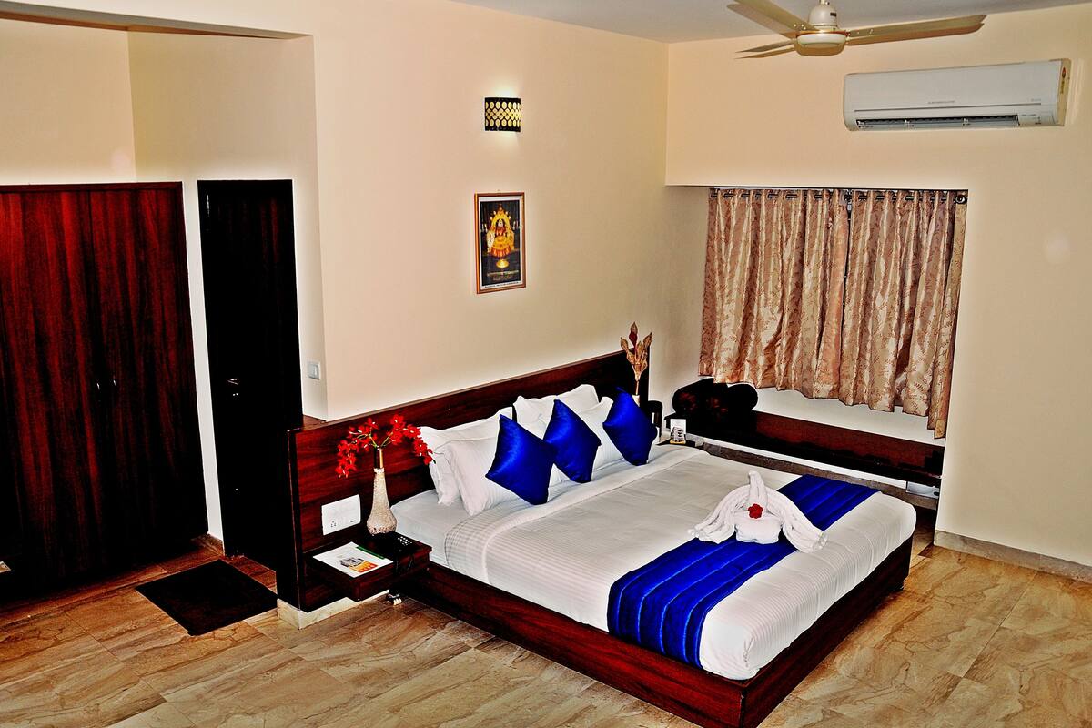 A hotel room with a bed, a nightstand, a desk, a window with curtains, a ceiling fan, and an air conditioning unit.
