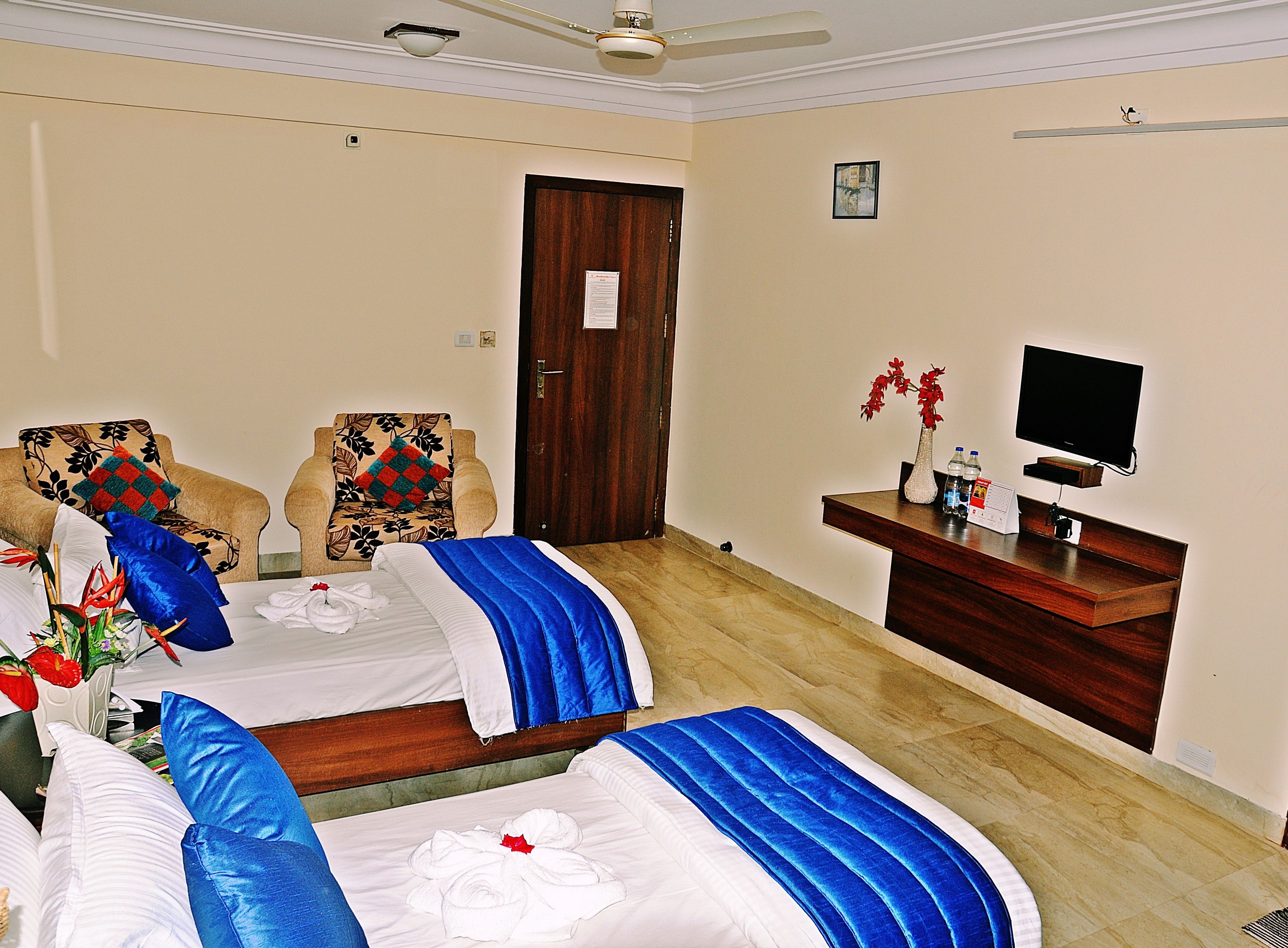 A hotel room with two beds, a TV, a desk, and a door.