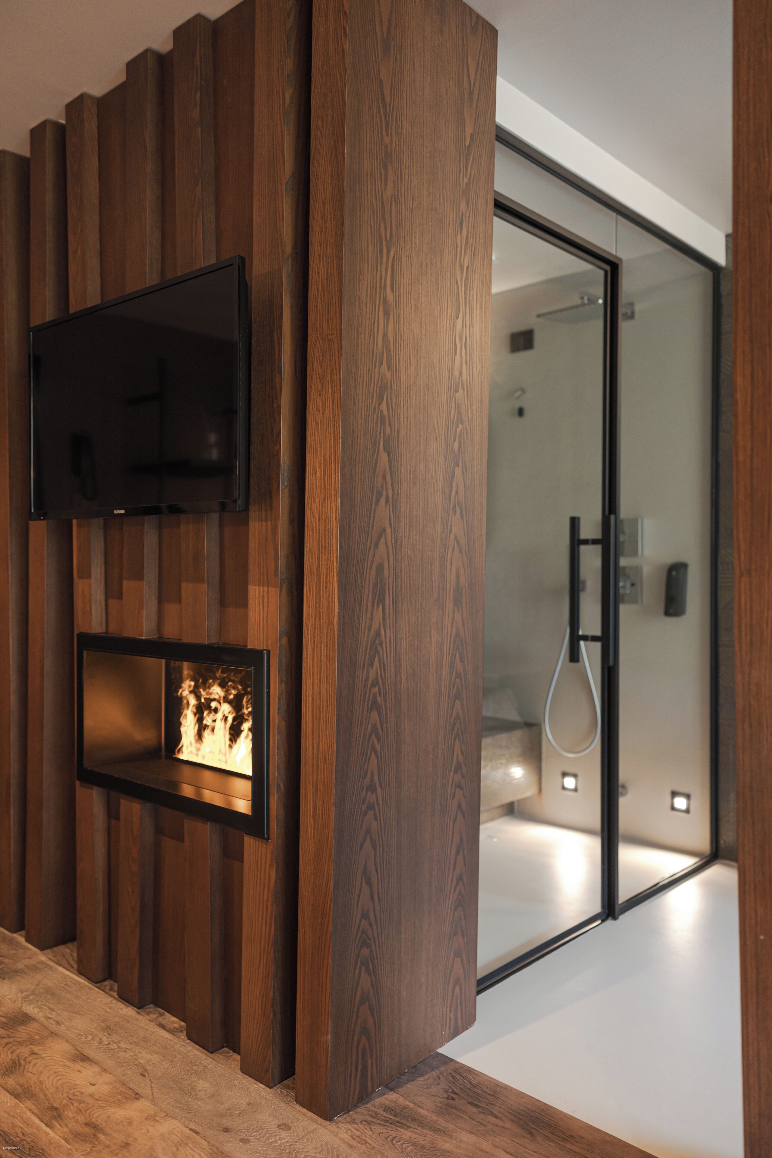 Une salle de bain moderne avec un mur recouvert de panneaux en bois, un téléviseur fixé au mur et une cabine de douche en verre.