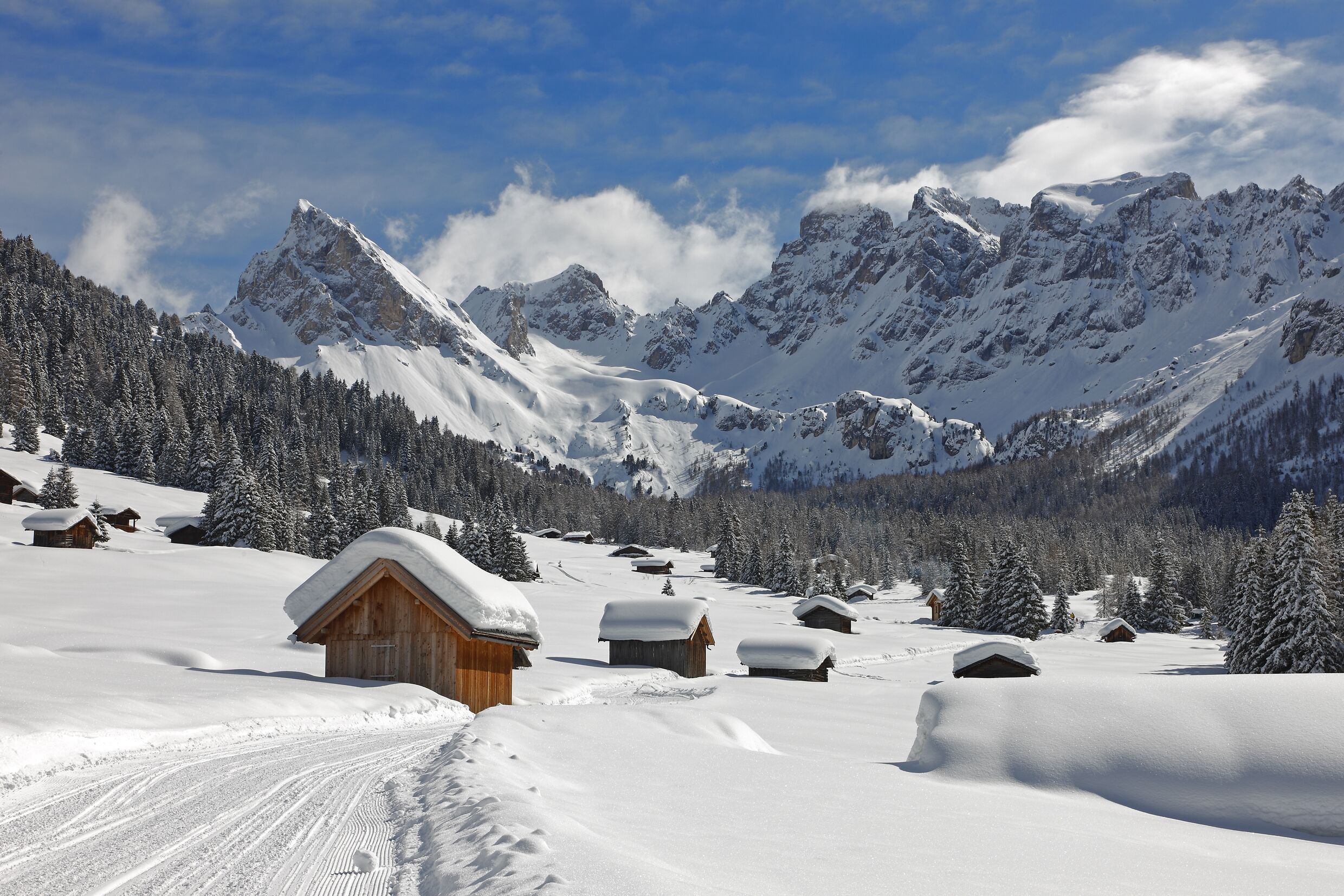 Schneebedeckte Berglandschaft mit Holzhütten und blauem Himmel.