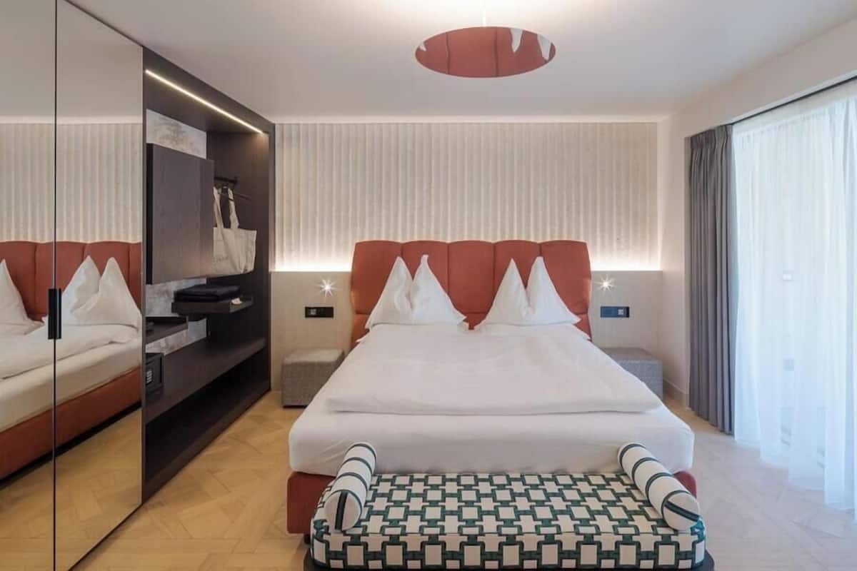Una camera d'albergo moderna con un letto grande, un comodino, un armadio e un'ampia finestra con tende.