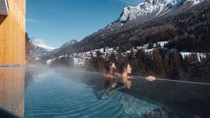 Vista despejada de una piscina con cubierta de madera, rodeada de montañas y árboles nevados.
