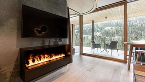 Una sala de estar moderna con un televisor de pantalla plana montado en la pared, una chimenea empotrada y grandes puertas correderas de vidrio que dan a un espacio exterior con vistas a un paisaje boscoso.