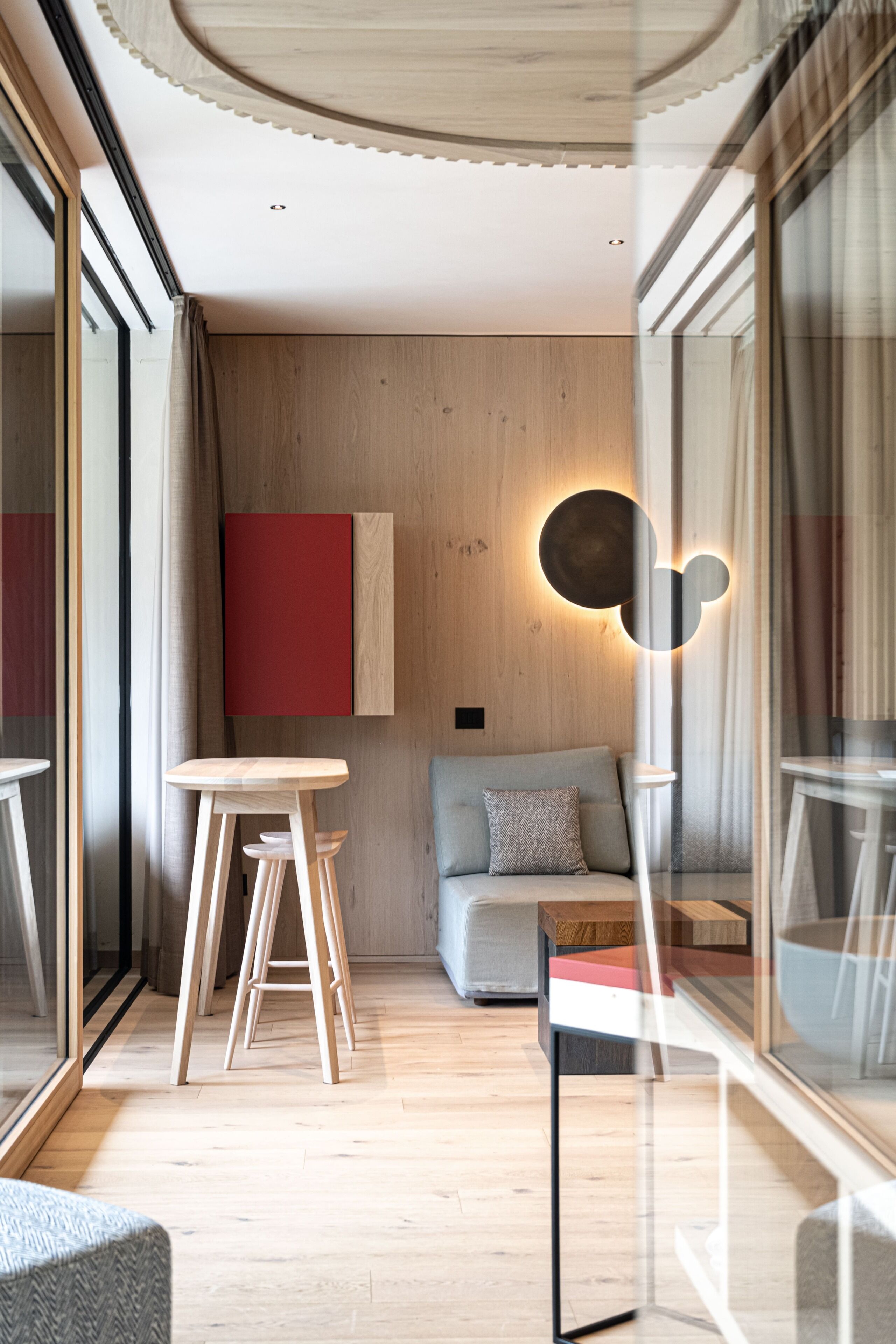Um interior moderno com piso de madeira, luminária redonda na parede, sofá e área de refeições com banquinhos.
