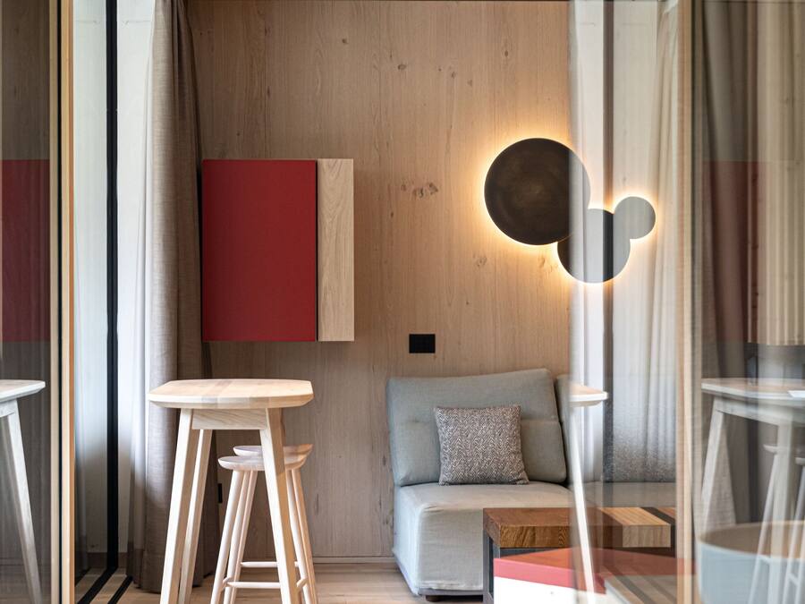 Um interior moderno com piso de madeira, luminária redonda na parede, sofá e área de refeições com banquinhos.