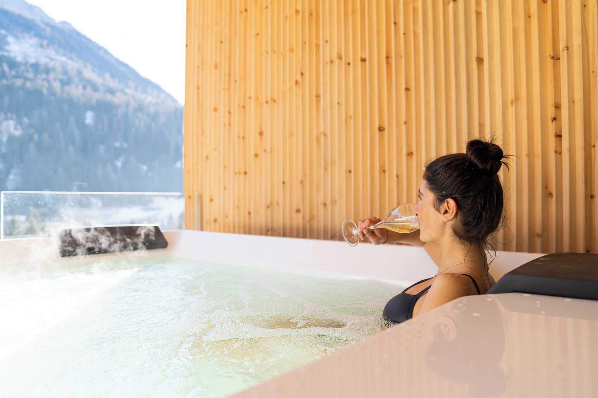 A person relaxing in a hot tub with a view of mountains.