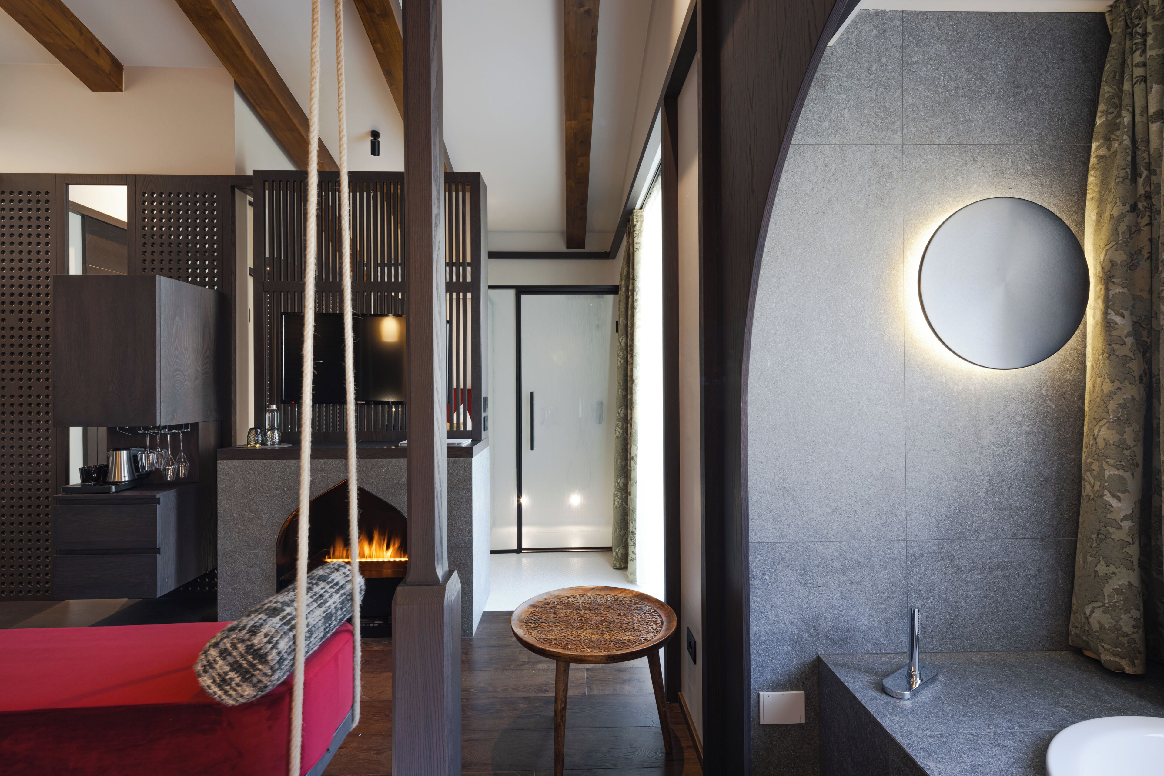 Ein modernes Interieur mit Kamin, rundem Spiegel und einem roten Sofa.
