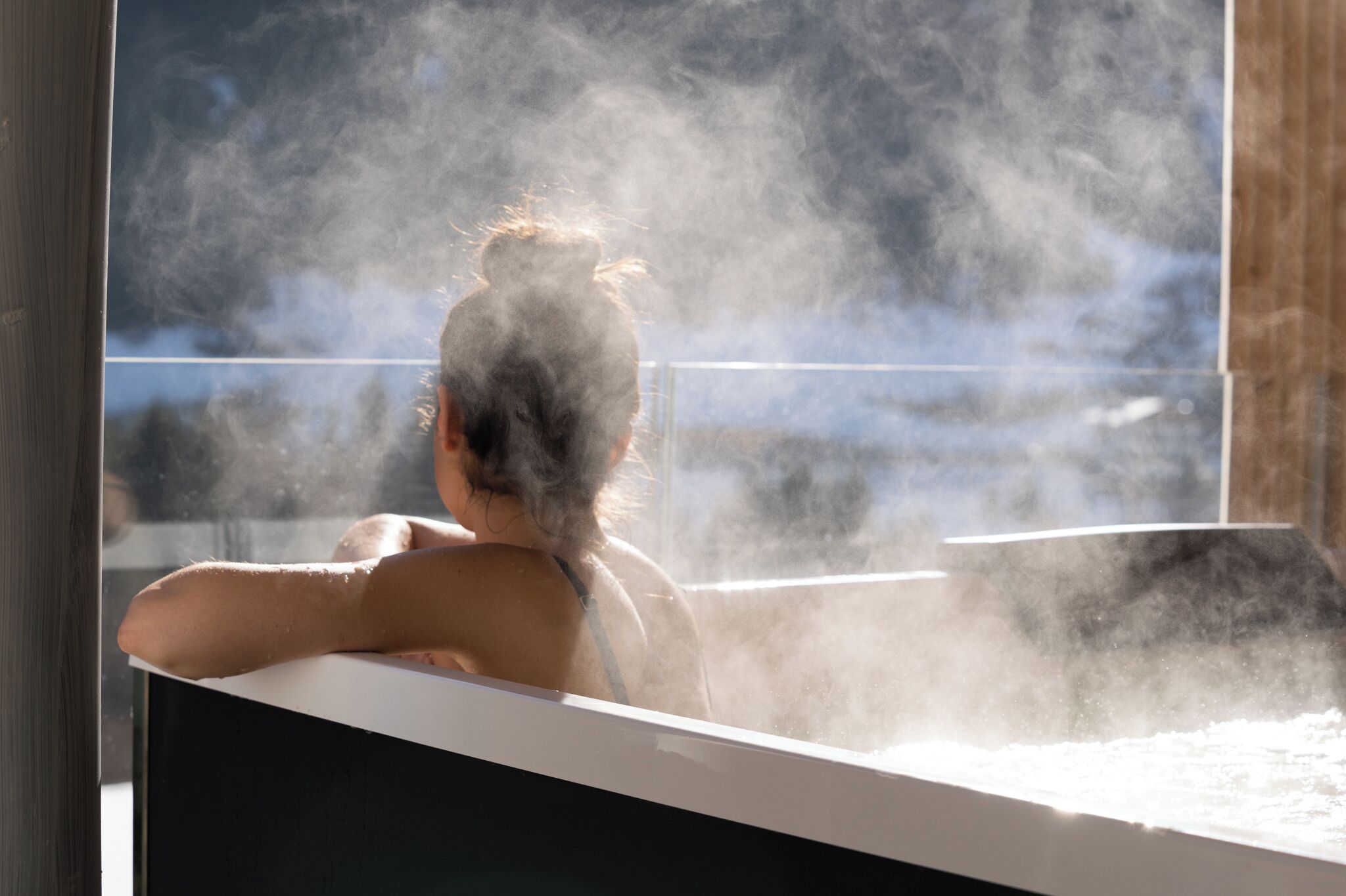 A person relaxing in a steam bath with a view of a snowy landscape.