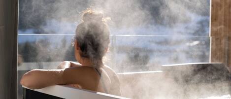 A person relaxing in a steam bath with a view of a snowy landscape.