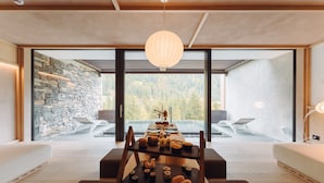 Un interior moderno con una mesa de comedor dispuesta para una comida, amplias ventanas que ofrecen vistas al exterior y una pared de piedra en un lateral.
