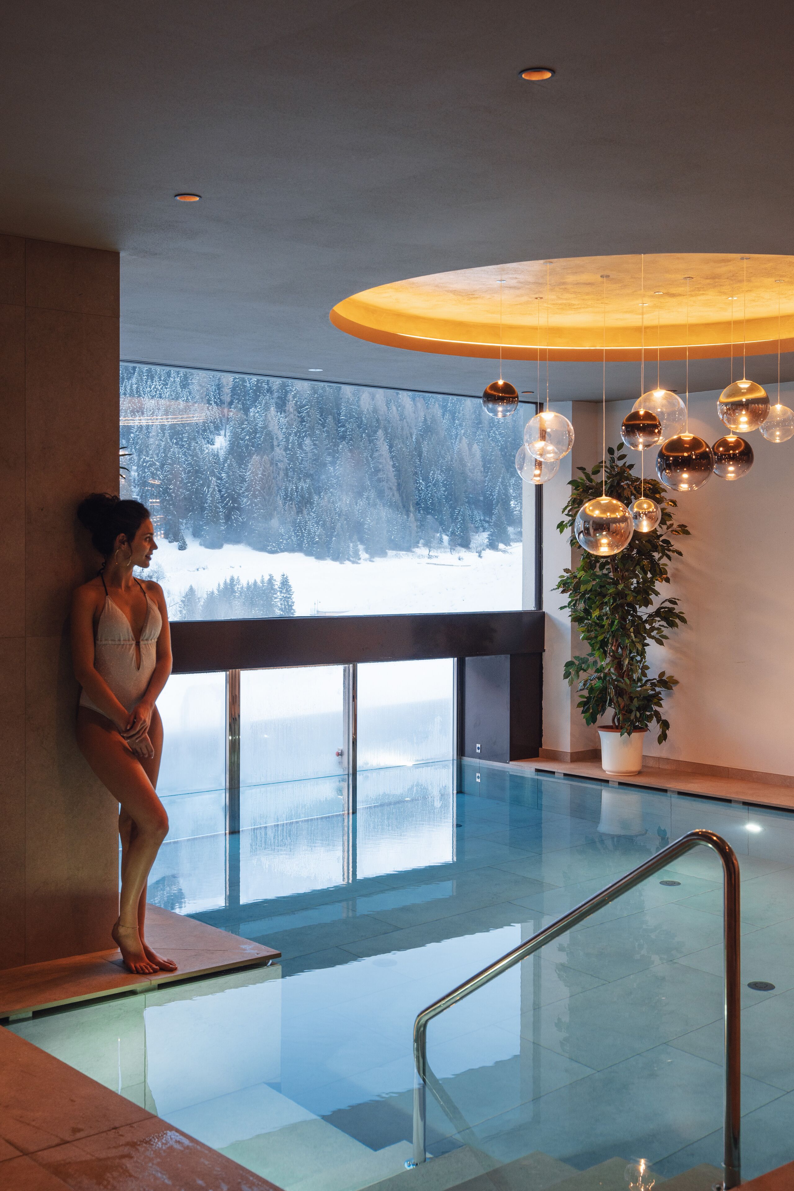 A woman standing by a pool with a view of a snowy landscape.