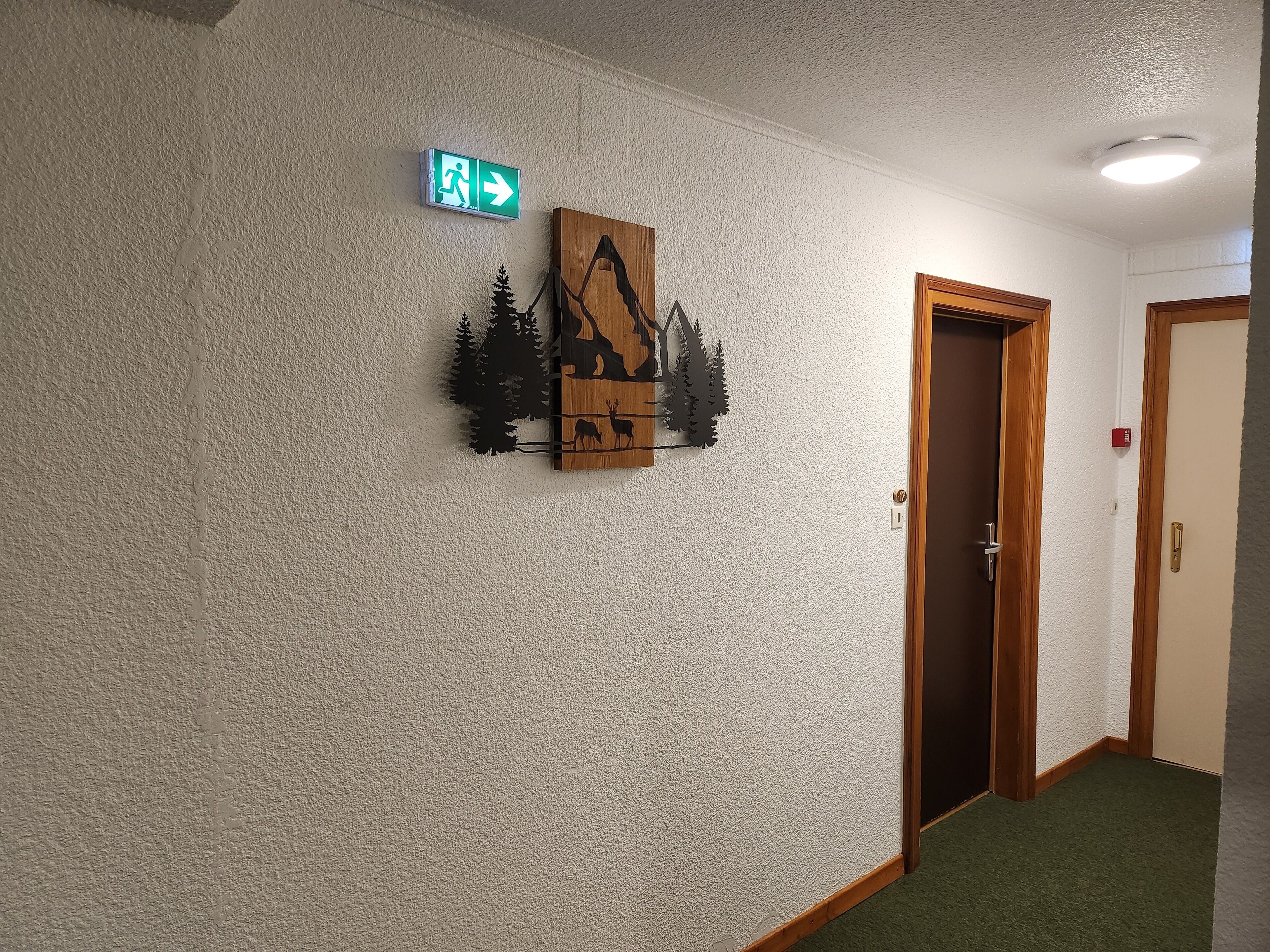 A hallway with a textured wall, a wooden decorative piece, and an exit sign.