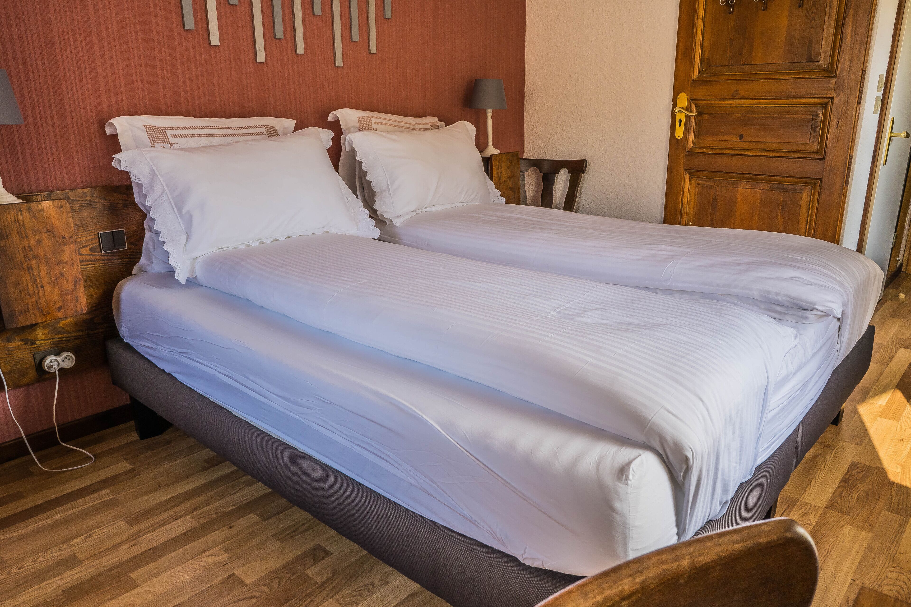 A neatly made bed with white linens, a wooden nightstand with a lamp, and a wooden door.