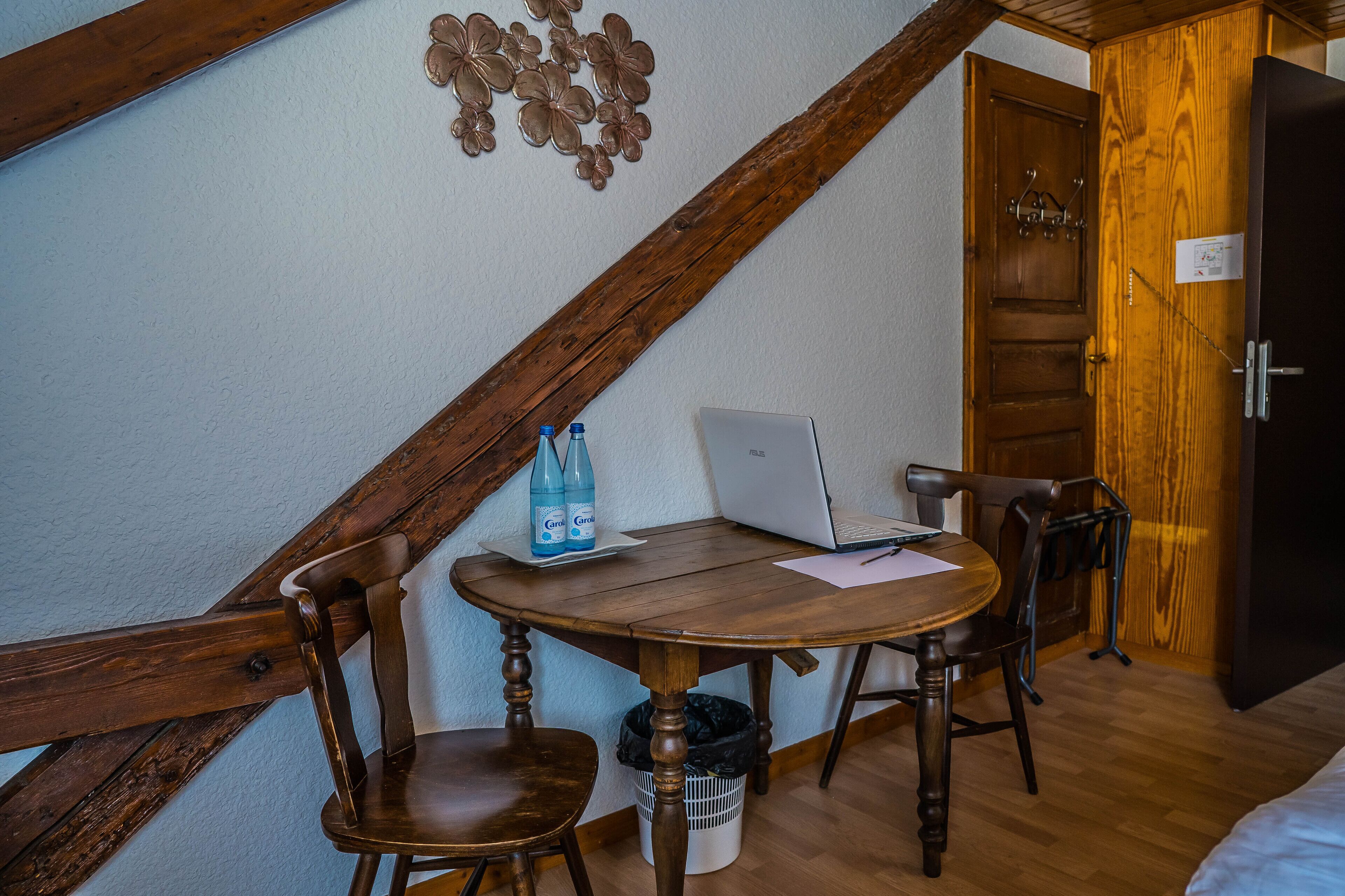Ein Zimmer mit einem Holztisch, zwei Stühlen, einem Laptop und einer Wasserflasche.