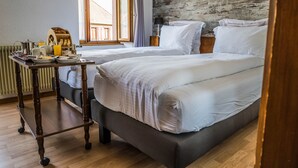 A hotel room with two beds, a wooden table with breakfast items, a radiator, and a large window with curtains. - Au Vieux Moulin (Lapoutroie)