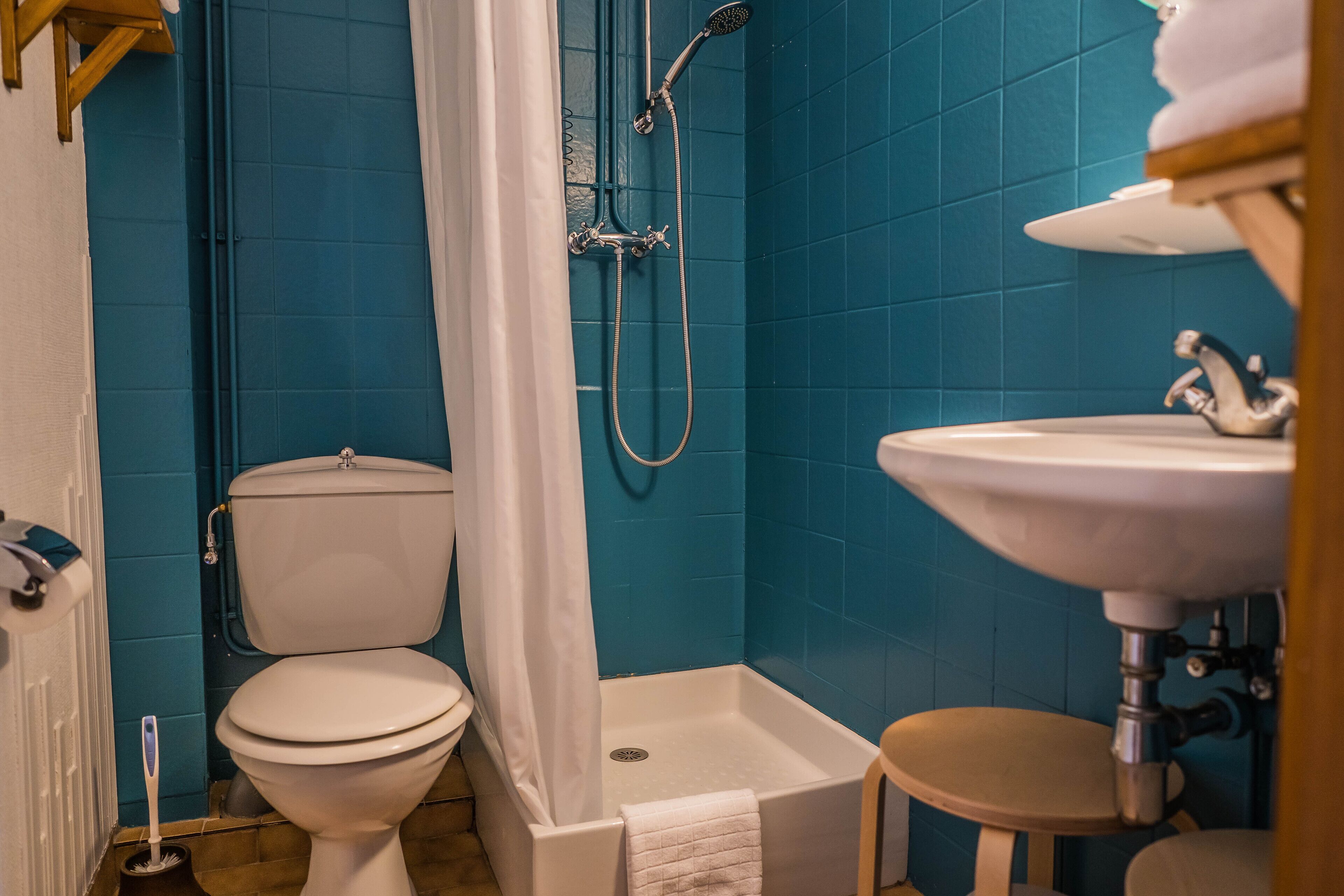 A bathroom with a toilet, shower, sink, and a small stool.