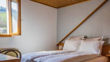 A bedroom with a bed, wooden headboard, bedside tables, and a window with a view of a house and greenery.