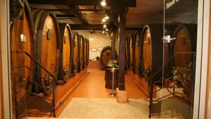 A wine cellar with wooden barrels arranged in rows, a central table with flowers, and a staircase leading to the upper level. - Au Vieux Moulin (Lapoutroie)