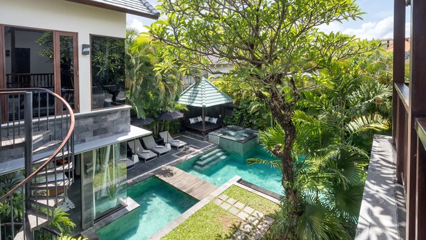Una casa moderna con piscina, mobiliario exterior y abundante vegetación.