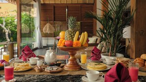 A breakfast setting with a fruit bowl, plates of food, and beverages. - Villa Desa Roro Dua by Villa Finder (Canggu)