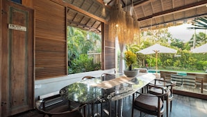 A wooden interior with a large dining table, chairs, and a hanging light fixture. - Villa Desa Roro Dua by Villa Finder (Canggu)