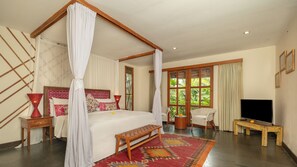 A four-poster bed with a canopy, a television, a bench, and a view of greenery through the windows. - Villa Desa Roro Dua by Villa Finder (Canggu)