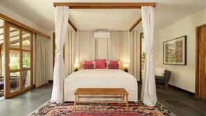 A four-poster bed with white linens and red pillows, a bench, a patterned rug, and a large window with curtains. - Villa Desa Roro Dua by Villa Finder (Canggu)