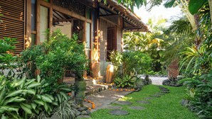 A traditional wooden house with a thatched roof, surrounded by lush greenery and a stone pathway. - Villa Desa Roro Dua by Villa Finder (Canggu)